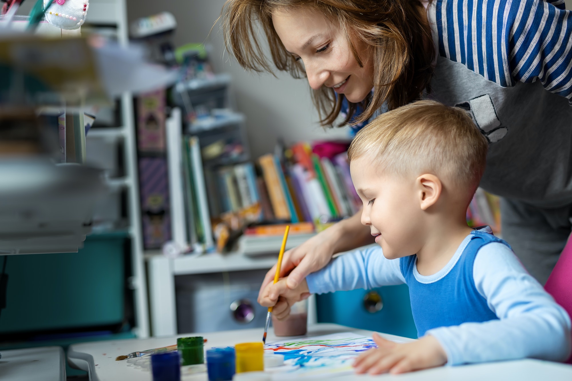 Young adult mom and cute little blond kid boy enjoy have fun painting with watercolor brush bright